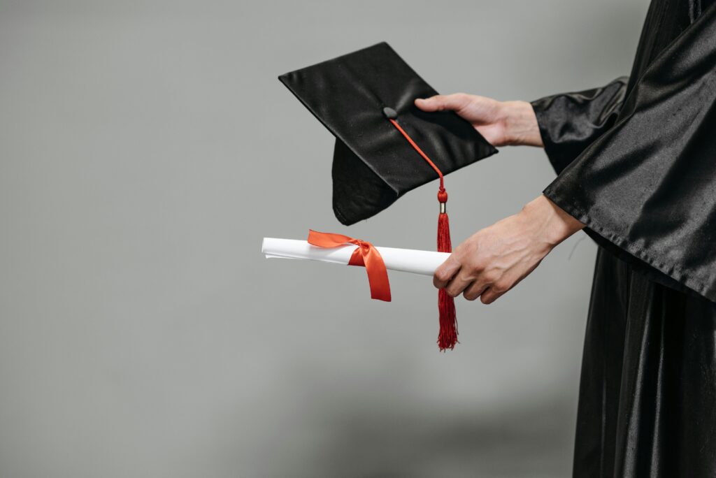 Close-up of graduate holding cap and diploma with red ribbon, symbolizing success.